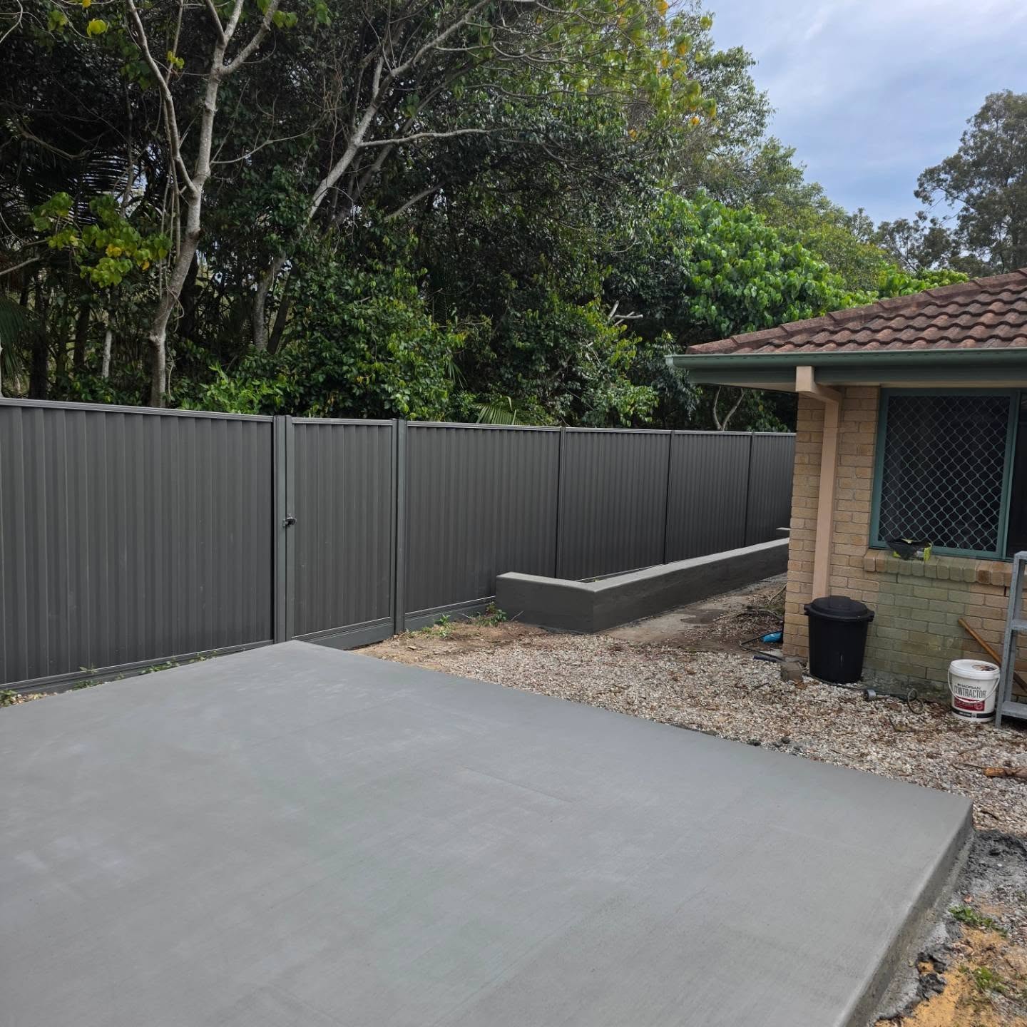 New smooth concrete slab in a backyard next to a dark grey fence