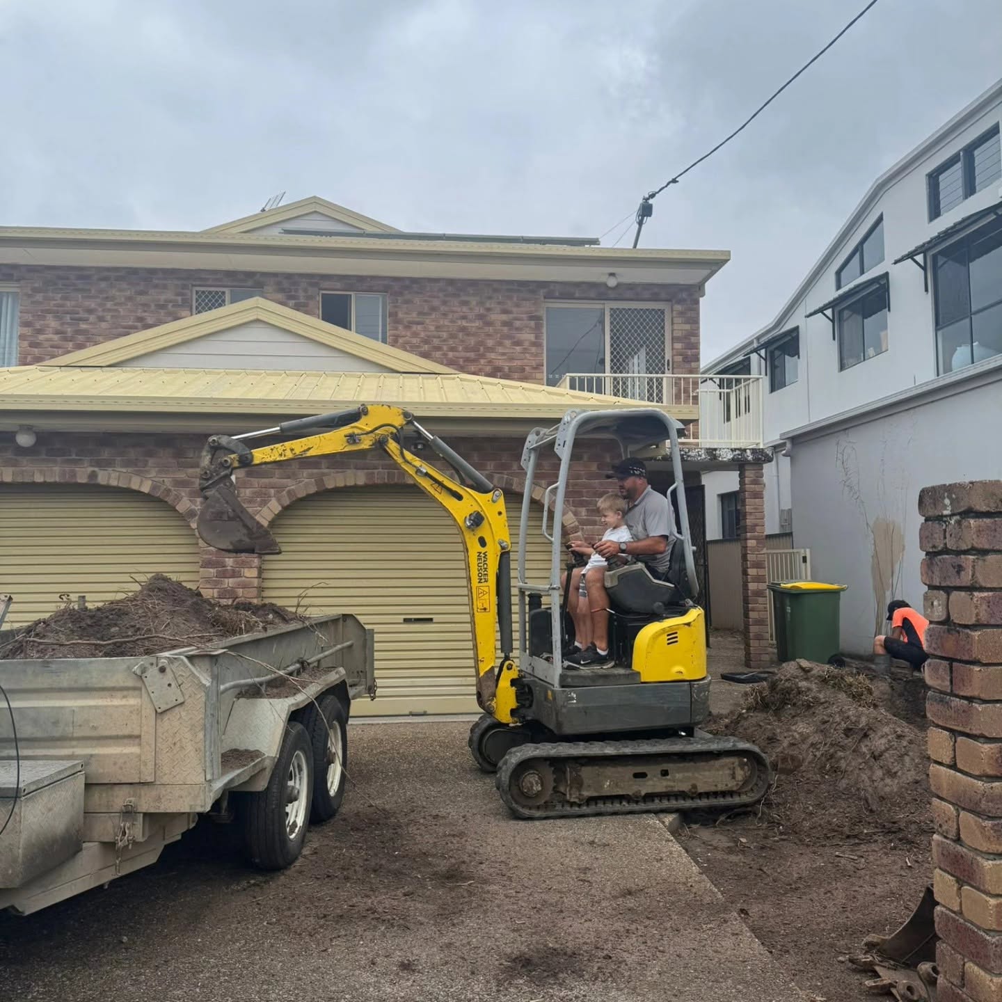 Az on the Azcon mini excavator digging out a driveway, with a trailer loaded with spoil